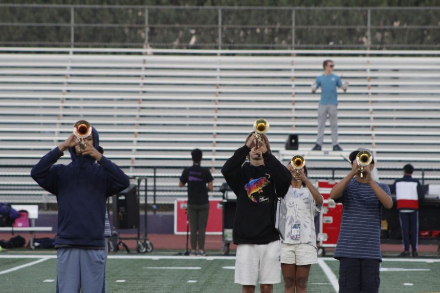 Trumpets performing with drum major in the background, making sure theyre in their perfect spots.