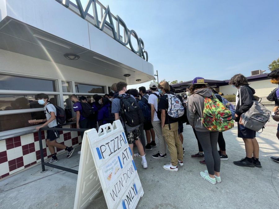 A huge group of students in the line squeeze their way to the small window to get their pizza.