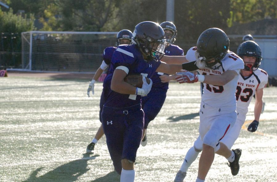 Amador football player dodges opposing team, grasping onto to the football.