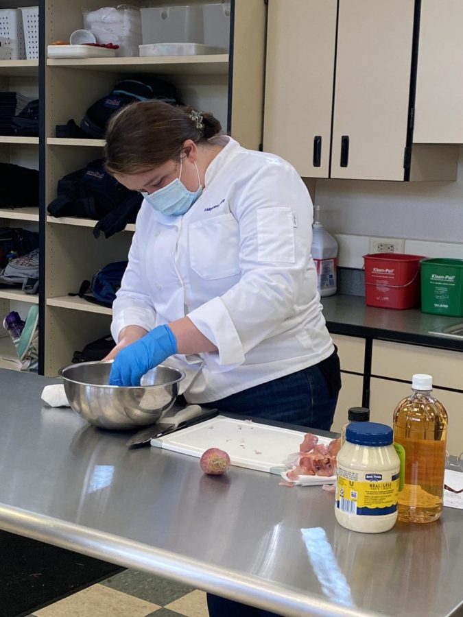 Allison Vincent ('22) cuts onions and puts them into the bowl. She is working on the main entree for a larger meal themed around Oktoberfest.
