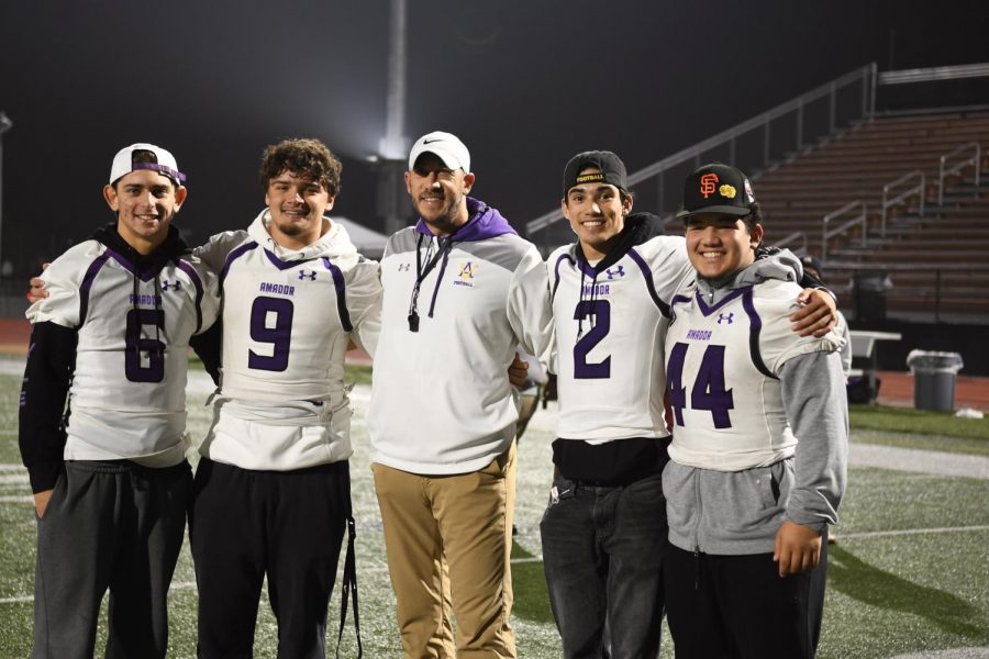 Four players smile with their coach in the middle.