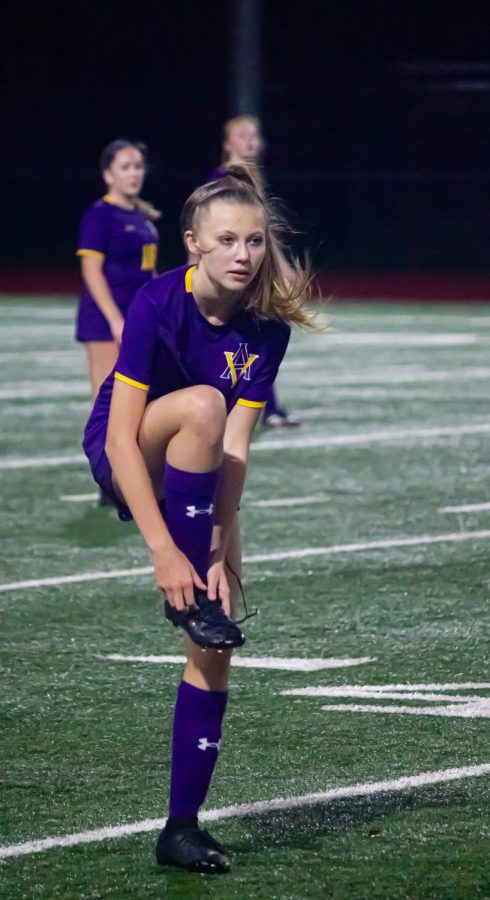 Brooklyn Harmon ('25) checks her cleats to prevent slipping on the wet field.
