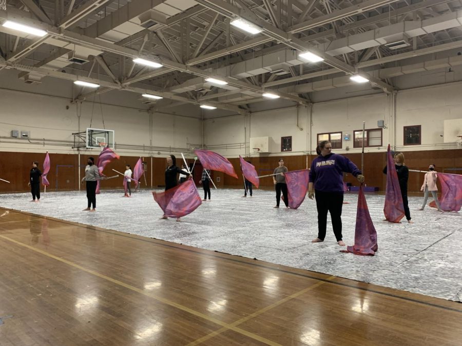 The+winterguard+practices+in+the+small+gym+with+their+flags+and+tarp.