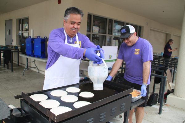 A volunteer chef dollops pancake batter on a stove.