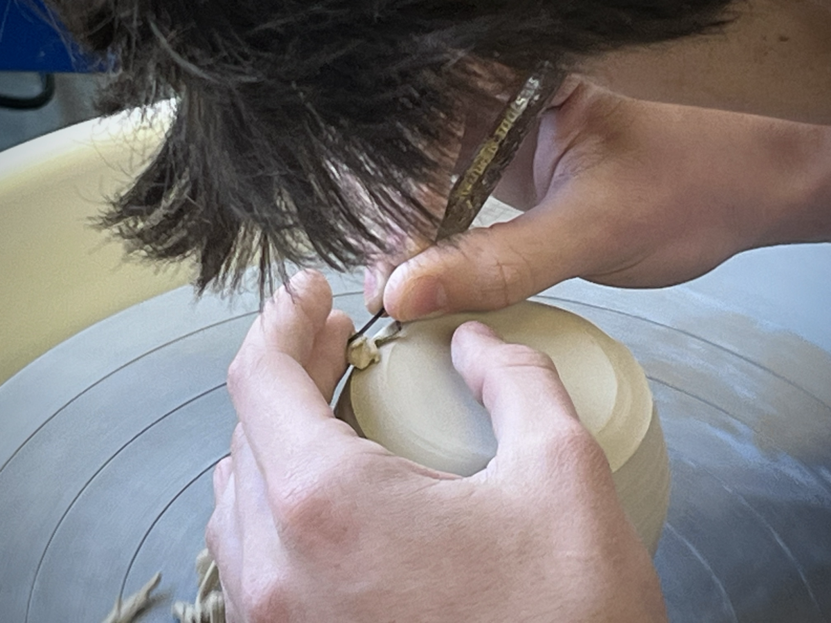 A student uses a potters wheel to shape the bottom of his cup.