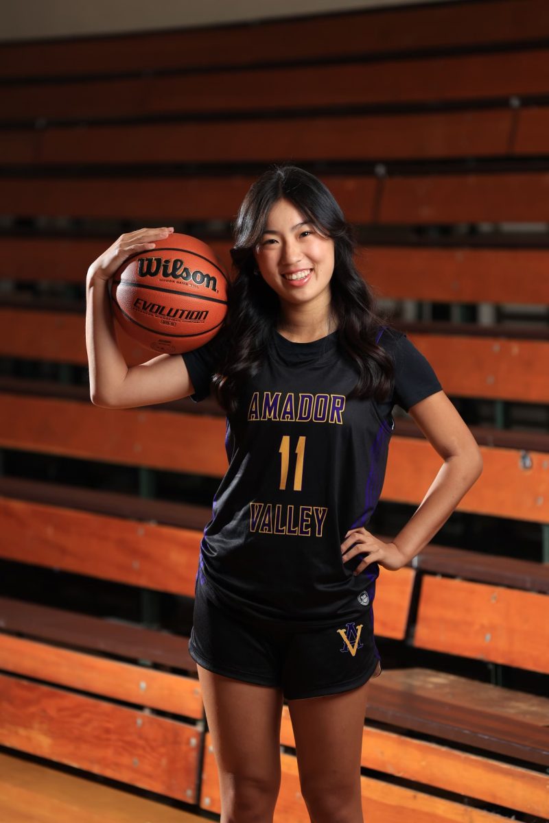 Senior Kacie Hu posing in her varsity uniform and with a basketball for annual sports portraits.