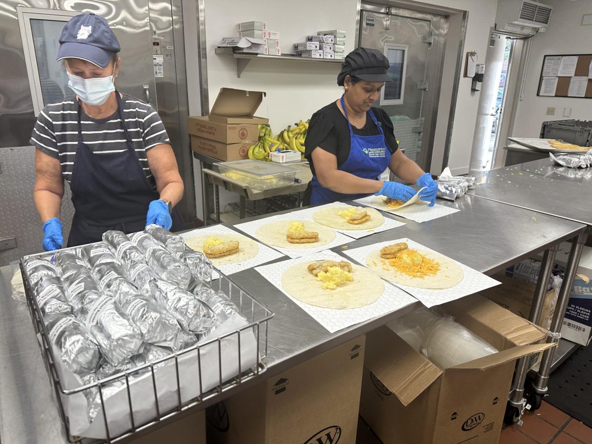 Amador lunch workers transfer warm food from cooking pans into disposable containers, carefully packaging them for lunchtime distribution.