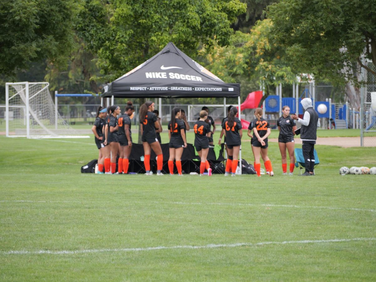 Girls RAGE Club Soccer gather around while Coach Liu instructs them during a game.