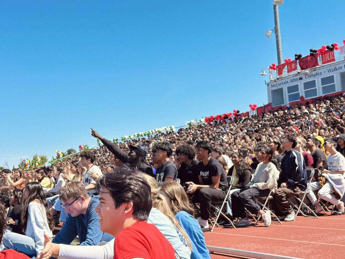 The crowd smiles and cheers on their classmates while keeping close track of the score. Lighthearted moments, such as a classmate tripping during an obstacle, add to the energy of the event.
