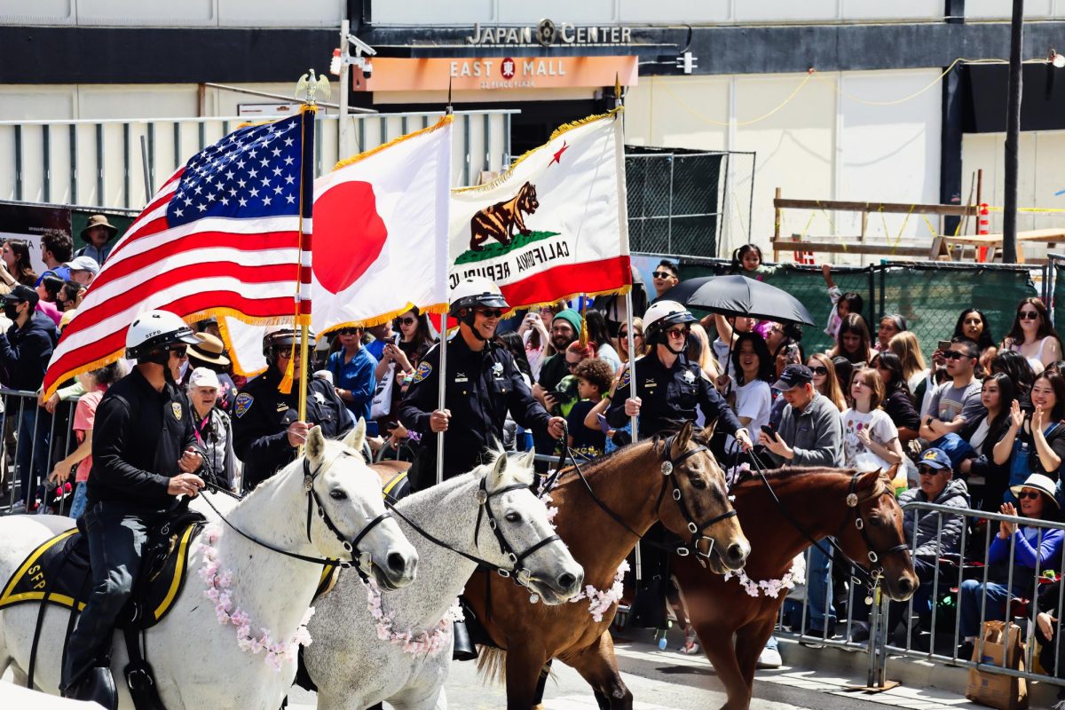 Mounted officers proudly ride down Post St. bearing US, Japanese, and California flags.