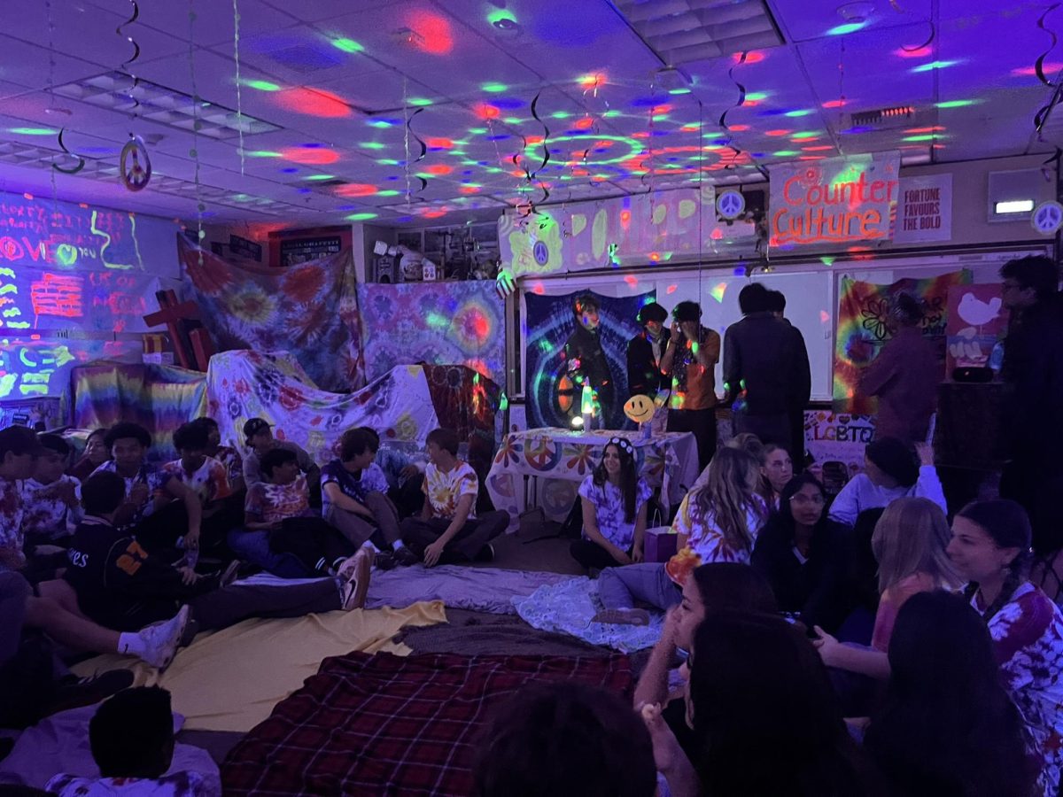 Juniors lounge around on blankets in a dimly-lit classroom, simulating the counterculture experience.